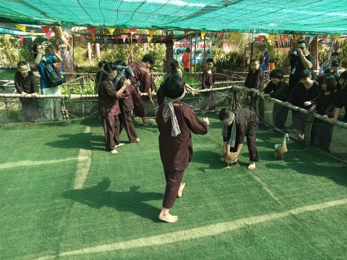 Ba bé mặc đồ nâu đang vây bắt vịt trong chuồng vịt rơm tại Dragon Farm